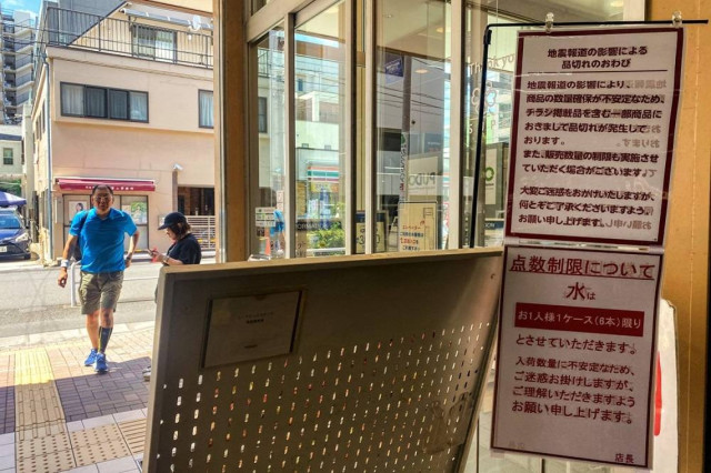 Customers walk by the entrance of a supermarket as signs written "quake-related media reports are causing some products to run out of stocks and that sales restrictions are likely" (up) and "bottled water is being rationed, with a cap of one case (six bot