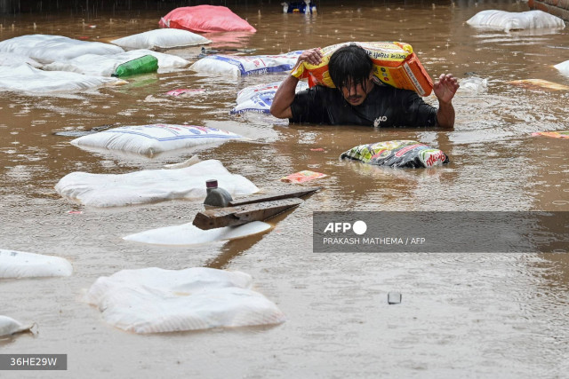 A man carrying a sack of flour wades through flood waters after the Bagmati River overflowed following heavy monsoon rains in Kathmandu on September 28, 2024. - Floods and landslides caused by heavy downpours in Nepal killed at least 10 people across the