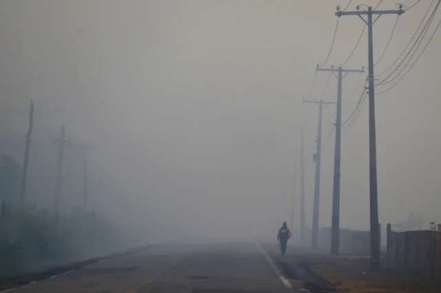 A person walks on the BR-319 highway through smoke from a forest fire that reaches Careiro Castanho in Brazil’s Amazonas state, Sept. 6, 2023.