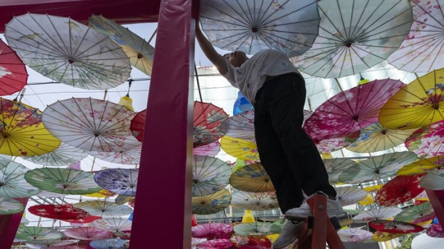 A worker sets up decorations formed with umbrellas for an outdoor market along the Wangfujing mall street in Beijing, Wednesday, June 19, 2024