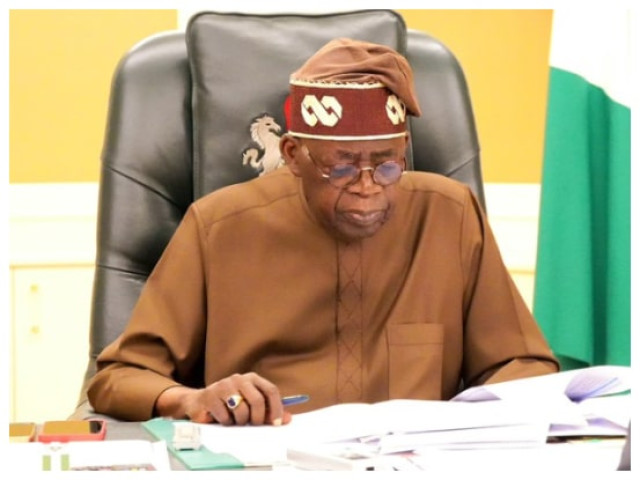 President Bola Tinubu was seated at his desk, wearing traditional attire and reading documents, with the Nigerian flag visible in the background.