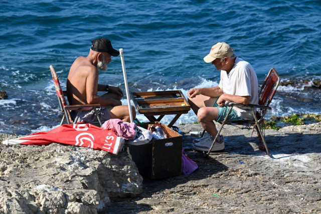 People play backgamon on a rock in Beirut's Ain al-Mreisseh seaside promenade on August 2, 2024